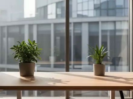 Ein minimalistischer, sonnendurchfluteter Büroarbeitsplatz mit einer einzelnen Pflanze und Blick auf eine moderne Fassade. - Foto: über boerse-global.de