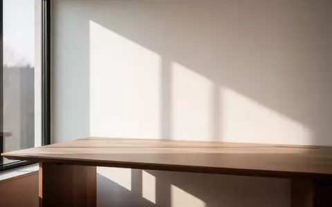 Ein minimalistischer Arbeitsplatz mit einem leeren Holztisch und natürlichem Sonnenlicht, das durch ein Fenster fällt. - Foto: über boerse-global.de