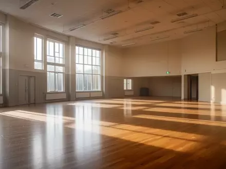 Ein heller, leerer Mehrzweckraum in einem Gemeindezentrum mit Holzboden und großen Fenstern bei Tageslicht. - Foto: über boerse-global.de