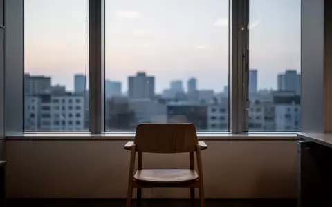 Ein ruhiges, minimalistisches Büro mit einem leeren Stuhl vor einem Fenster mit Blick auf eine abendliche Stadtkulisse. - Foto: über boerse-global.de