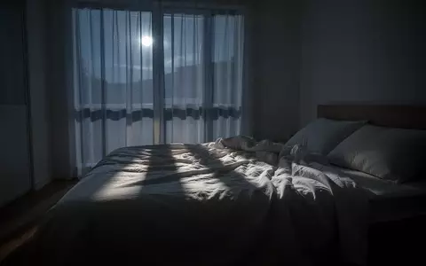 Ein minimalistisch eingerichtetes Schlafzimmer in der Nacht mit sanftem Mondlicht, das durch Vorhänge auf ein ungemachtes Bett fällt. - Foto: über boerse-global.de