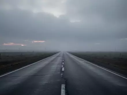 Eine menschenleere, graue Autobahn erstreckt sich in die neblige Ferne unter einem bewölkten Himmel. - Foto: über boerse-global.de