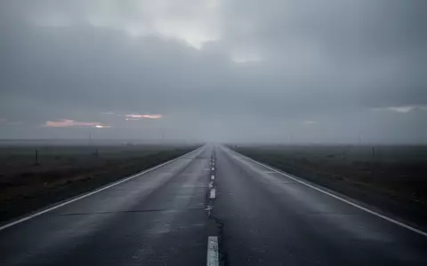 Eine menschenleere, graue Autobahn erstreckt sich in die neblige Ferne unter einem bewölkten Himmel. - Foto: über boerse-global.de