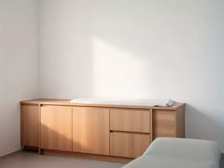 Ein minimalistischer, heller Behandlungsraum in einer Arztpraxis mit Fokus auf eine schlichte Wand und Tageslicht. - Foto: über boerse-global.de