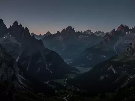 Eine weite, ruhige Berglandschaft in der Abenddämmerung mit scharfen Felsformationen und tiefen Schatten unter einem klaren Himmel. - Foto: über boerse-global.de