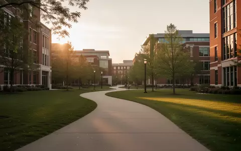 Ein ruhiger, gepflasterter Fußweg auf einem modernen Universitätsgelände bei goldenem Licht, umgeben von gepflegten Grünflächen und Backsteingebäuden. - Foto: über boerse-global.de