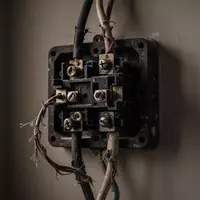 Nahaufnahme von verschlissenen, elektrischen Leitungen und einer veralteten Abzweigdose an einer schlichten Wand. - Foto: über boerse-global.de