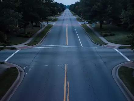 Eine leere, ruhige Vorstadtstraße in der Dämmerung mit asphaltierter Fahrbahn und angrenzenden Grünflächen ohne Personen oder Fahrzeuge. - Foto: über boerse-global.de