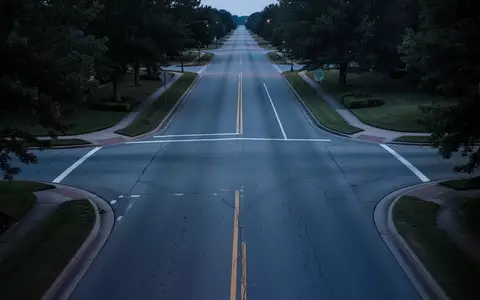 Eine leere, ruhige Vorstadtstraße in der Dämmerung mit asphaltierter Fahrbahn und angrenzenden Grünflächen ohne Personen oder Fahrzeuge. - Foto: über boerse-global.de
