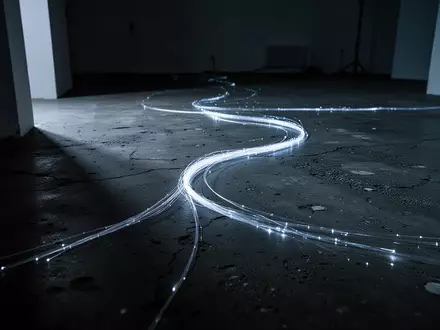 Ein einzelnes leuchtendes Glasfaserkabel auf einem rauen Betonboden in einer dunklen, minimalistischen Umgebung. - Foto: über boerse-global.de