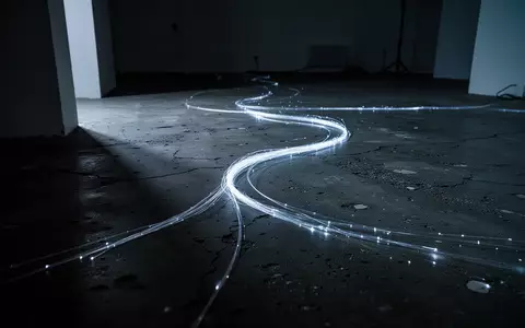 Ein einzelnes leuchtendes Glasfaserkabel auf einem rauen Betonboden in einer dunklen, minimalistischen Umgebung. - Foto: über boerse-global.de