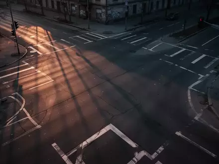 Eine leere, dunkle Straßenkreuzung in der Dämmerung mit langen Schatten und geometrischen Bodenmarkierungen. - Foto: über boerse-global.de