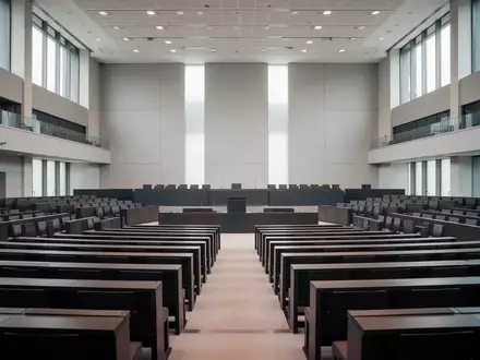 Leerer Plenarsaal des Deutschen Bundestages mit Fokus auf die Architektur und die hölzernen Sitzreihen bei natürlichem Licht. - Foto: über boerse-global.de
