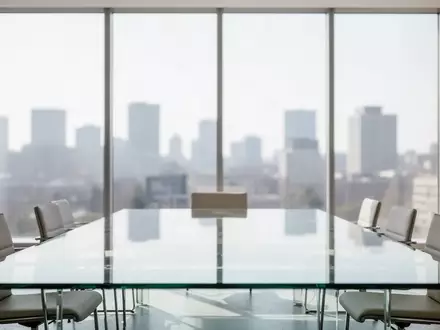 Ein minimalistischer, leerer Konferenzraum mit einem gläsernen Tisch und großen Fenstern bei Tageslicht. - Foto: über boerse-global.de