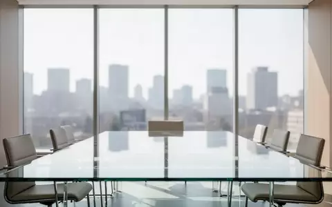 Ein minimalistischer, leerer Konferenzraum mit einem gläsernen Tisch und großen Fenstern bei Tageslicht. - Foto: über boerse-global.de
