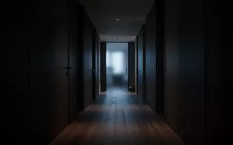 Ein dunkler, leerer Flur in einer modernen Wohnung bei Nacht, der auf eine entfernte, schwach beleuchtete Tür zuführt. - Foto: über boerse-global.de
