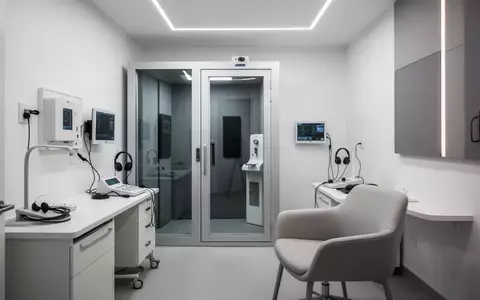 Ein minimalistisch eingerichteter, moderner Audiometrie-Raum mit einer schallisolierten Prüfkabine in einer klinischen Umgebung. - Foto: über boerse-global.de