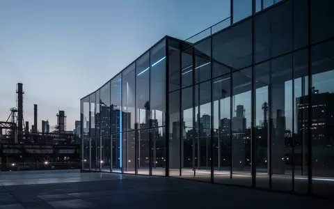 Moderne Glas- und Stahlarchitektur bei Dämmerung vor einem industriellen Stadtbild. - Foto: über boerse-global.de