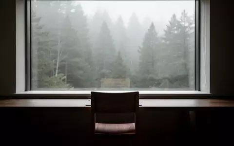 Ein minimalistischer, ruhiger Arbeitsraum mit einem leeren Stuhl vor einem Fenster, das auf einen nebligen Wald blickt. - Foto: über boerse-global.de