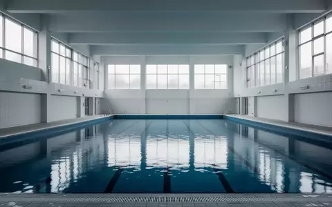 Ein leeres kommunales Hallenbad mit blauem Wasser und hellen Fliesen in einer modernen, minimalistischen Architektur. - Foto: über boerse-global.de