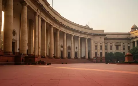 Die Fassade eines neoklassizistischen Regierungsgebäudes in New Delhi bei goldenem Licht mit großen Steinsäulen und einem leeren Vorplatz. - Foto: über boerse-global.de