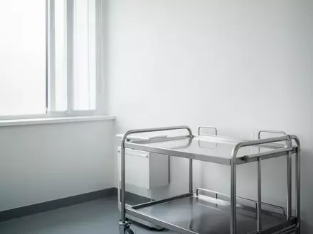 Ein heller, minimalistischer Behandlungsraum in einer Kinderarztpraxis mit einem leeren medizinischen Rollwagen. - Foto: über boerse-global.de