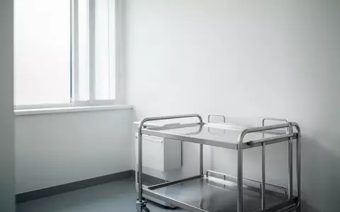 Ein heller, minimalistischer Behandlungsraum in einer Kinderarztpraxis mit einem leeren medizinischen Rollwagen. - Foto: über boerse-global.de