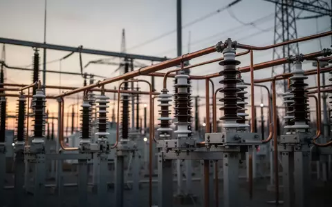 Hochspannungs-Umspannstation mit Kupfer-Sammelschienen und Keramikisolatoren vor einem verschwommenen industriellen Hintergrund. - Foto: über boerse-global.de