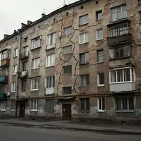 Fassade eines sanierungsbedürftigen Wohnhauses mit sichtbaren Rissen im Mauerwerk bei bewölktem Himmel. - Foto: über boerse-global.de