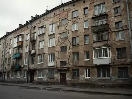 Fassade eines sanierungsbedürftigen Wohnhauses mit sichtbaren Rissen im Mauerwerk bei bewölktem Himmel. - Foto: über boerse-global.de