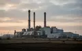 Industrieanlage mit hohen Schornsteinen und Metallgebäuden in einer ländlichen Umgebung bei bewölktem Himmel. - Foto: über boerse-global.de