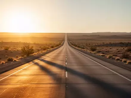 Eine weitläufige, leere Autobahn in einer sonnendurchfluteten Wüstenlandschaft während der goldenen Stunde. - Foto: über boerse-global.de