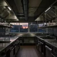 Leere, professionelle Gastronomieküche mit Edelstahl-Oberflächen und Abzugshauben in einer schummrigen Lichtstimmung. - Foto: über boerse-global.de