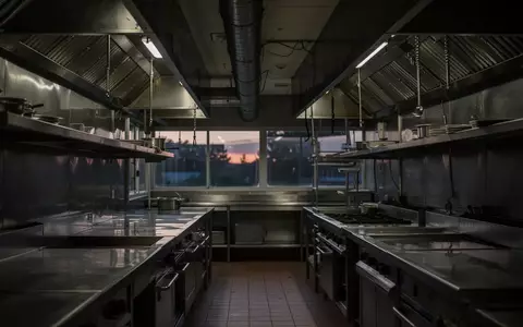 Leere, professionelle GastronomiekĂŒche mit Edelstahl-OberflĂ€chen und Abzugshauben in einer schummrigen Lichtstimmung. - Foto: ĂŒber boerse-global.de