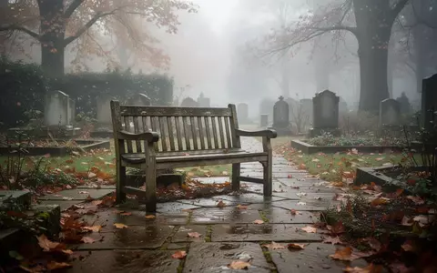 Ein einsamer, verwitterter Holzbank in einem stillen Friedhofsgarten an einem nebligen Herbstmorgen. - Foto: über boerse-global.de