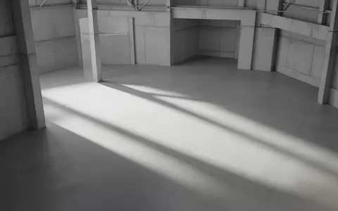 Minimalistische, leerstehende Industriehalle mit klaren geometrischen Schattenwürfen auf einem Betonboden. - Foto: über boerse-global.de