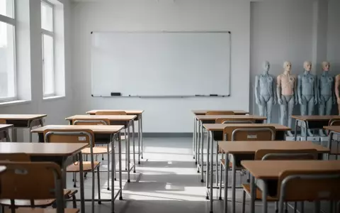Leere Schulbänke in einem hellen Klassenzimmer, im Hintergrund stehen Reanimationspuppen für das Erste-Hilfe-Training bereit. - Foto: über boerse-global.de