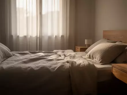 Ein minimalistisch eingerichtetes Schlafzimmer in sanftem Morgenlicht mit einem unbenutzten, ordentlich gemachten Bett. - Foto: über boerse-global.de