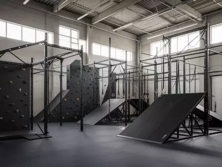 Moderne, leere Trainingshalle mit Hindernisparcours, Kletterstrukturen und Stahlrampen in einer hellen Industriehalle. - Foto: über boerse-global.de