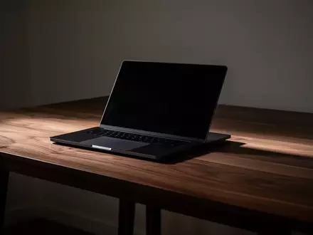 Ein geschlossener Laptop auf einem schlichten Holztisch in einem schwach beleuchteten Raum. - Foto: über boerse-global.de