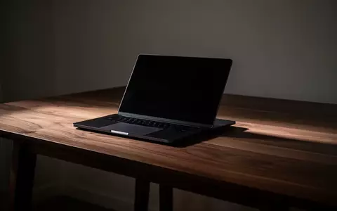 Ein geschlossener Laptop auf einem schlichten Holztisch in einem schwach beleuchteten Raum. - Foto: über boerse-global.de