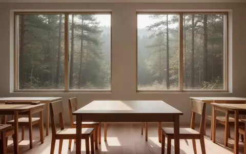 Ein heller, minimalistischer Klassenraum mit Holztischen und Blick auf einen ruhigen Wald, der eine Atmosphäre von Ruhe und Ausgeglichenheit vermittelt. - Foto: über boerse-global.de