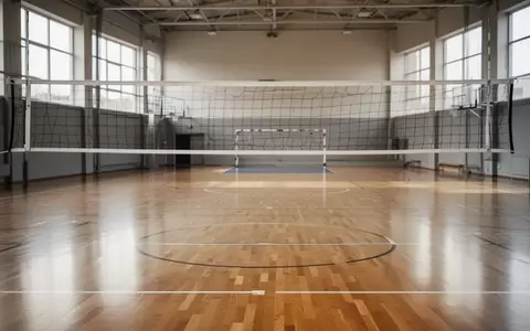 Ein leeres Volleyballnetz in einer hellen, modernen Sporthalle mit Parkettboden. - Foto: über boerse-global.de