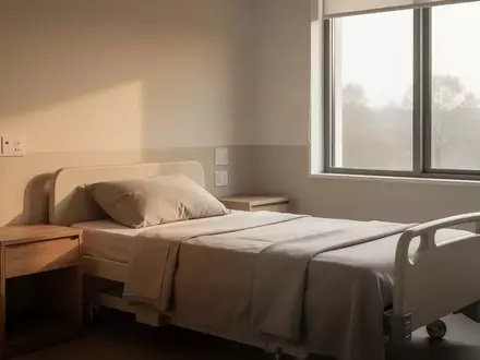 Ein minimalistisch eingerichtetes, helles Pflegezimmer mit einem ordentlich gemachten Bett und Tageslichteinfall. - Foto: über boerse-global.de
