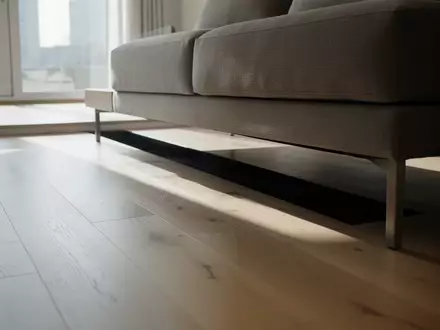 Ein minimalistisch gestalteter Wohnbereich mit hellem Holzboden und einem niedrigen Sofa, das einen freien Raum unter sich lässt. - Foto: über boerse-global.de