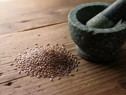 Dunkle Leinsamen neben einem Mörser aus Stein auf einem rustikalen Holztisch. - Foto: über boerse-global.de