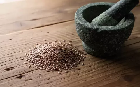 Dunkle Leinsamen neben einem Mörser aus Stein auf einem rustikalen Holztisch. - Foto: über boerse-global.de