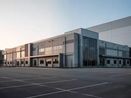 Ein großflächiger, moderner Gewerbebau mit weitläufiger asphaltierter Fläche bei klarem Tageslicht. - Foto: über boerse-global.de