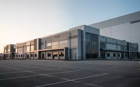 Ein großflächiger, moderner Gewerbebau mit weitläufiger asphaltierter Fläche bei klarem Tageslicht. - Foto: über boerse-global.de