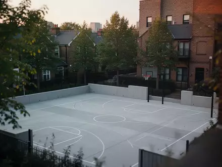 Ein moderner, menschenleerer Sportplatz in einem Wohnviertel bei Dämmerung, umgeben von Bäumen und Architektur. - Foto: über boerse-global.de